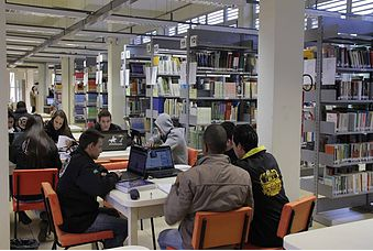 Foto da parte interna da biblioteca - estantes e mesa com alunos